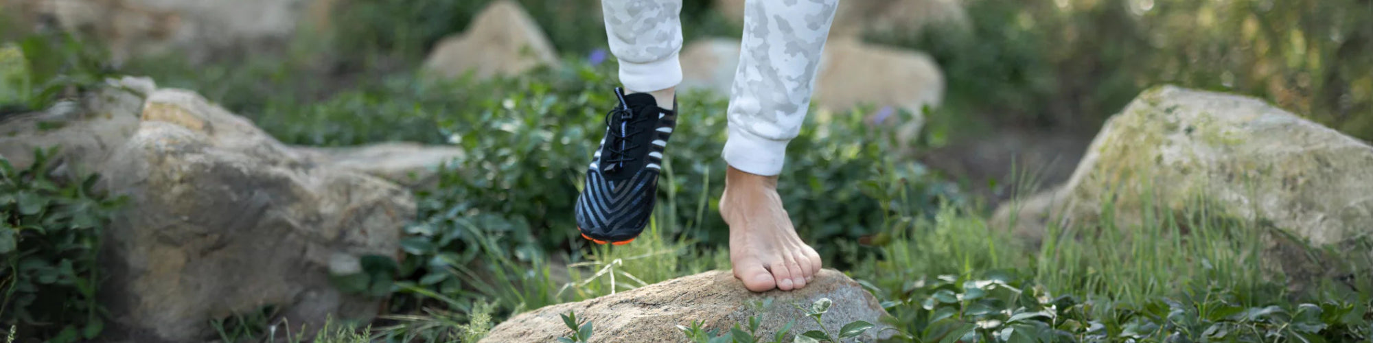 Vue panoramique d’une chaussure barefoot Grounda de la marque Yuhmae portée par un sportif en pleine marche pieds nus sur un sentier naturel. Modèle ultra flexible et léger conçu pour respecter la posture naturelle du pied, offrant un confort optimal et une liberté de mouvement totale. Idéal pour les amateurs de randonnée, trail et marche naturelle, cette chaussure minimaliste améliore l’équilibre et la stabilité tout en protégeant efficacement le pied sur terrains variés.